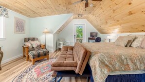A bedroom with a wooden ceiling, a bed, a sofa, a chair, a lamp, and a television. - Introducing our new Waterfront Hideaway Studio  (Palm City)