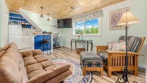 A cozy living room with a sofa, a wooden chair, and a dining table. There is a kitchen area with a microwave and a sink. - Introducing our new Waterfront Hideaway Studio  (Palm City)