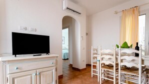 A room with a TV on a cabinet, a dining area with chairs, and a window with curtains.