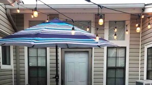 A patio with a striped umbrella, a table, and four chairs. - Heroes Boulevard House with room for up to ten (Lawton)