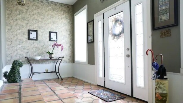 A hallway with patterned walls, a tiled floor, a small table with a vase and orchid, and a door with a decorative handle. - Heroes Boulevard House with room for up to ten (Lawton)