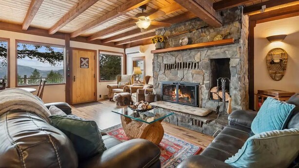 A cozy living room with a stone fireplace, leather sofas, and a view of the outdoors. - Big Mountain Treehouse!  Beautiful cabin home w/ SPECTACULAR views of Lake (Whitefish)