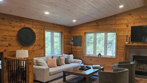 A cozy room with a sofa, a coffee table, a fireplace, and a TV. - Cabin with hot tub, heated swimming pool and acres of backyard hiking  (Adams)