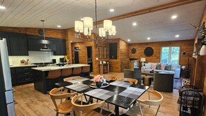 A modern kitchen with a central island, dining area with a black table and chairs, and a cozy living area with a sofa and a coffee table. - Cabin with hot tub, heated swimming pool and acres of backyard hiking  (Adams)