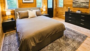 A bedroom with a large bed, wooden walls, a ceiling fan, and framed artwork. - Cabin with hot tub, heated swimming pool and acres of backyard hiking  (Adams)
