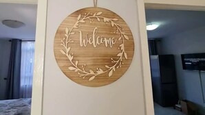 A circular wooden wall decoration with the word "Welcome" surrounded by a laurel wreath, mounted on a white wall. - Heritage Self Catering Apartment<br>Home from Home (Harare)