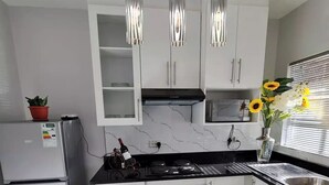 A modern kitchen with white cabinets, a stainless steel refrigerator, a black stove, and a built-in oven. There are hanging pendant lights and a vase with flowers on the counter. - Heritage Self Catering Apartment<br>Home from Home (Harare)