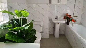 A bathroom with a toilet, sink, and bathtub. There is a cabinet above the sink and a plant next to the toilet. - Heritage Self Catering Apartment<br>Home from Home (Harare)