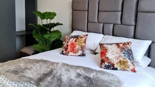 A bed with a grey fur throw, two decorative pillows, and a grey headboard. - Heritage Self Catering Apartment<br>Home from Home (Harare)