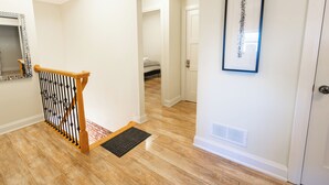 Un couloir avec un escalier en bois, un tableau encadré au mur et une porte au fond.