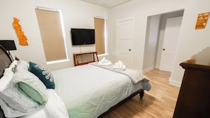 Un lit bien fait, avec une couette blanche et des oreillers, un téléviseur fixé au mur et un plancher en bois.