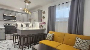 A modern kitchen with a central island, grey cabinets, and a yellow sofa with patterned cushions.