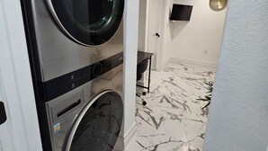A laundry room with a wall-mounted washer and dryer, a clock on the wall, and a marble-patterned floor.