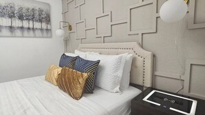 A modern bedroom with a geometric-patterned headboard, a bedside table with a control panel, and a wall-mounted lamp.