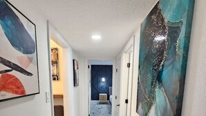 Un pasillo con suelo de mármol, paredes blancas y obras de arte a los lados.