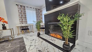 Una sala de estar moderna con chimenea, un televisor de pantalla plana y dos plantas en macetas.