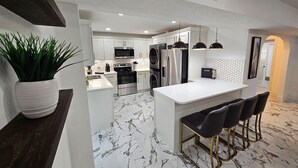 Una cocina moderna con armarios blancos, piso de mármol y una isla central con taburetes de bar.