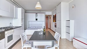 A modern kitchen with white cabinets, a stove, and a dining area with a table and chairs. - Lydie apt. exclusive holigarda (Desenzano del Garda)