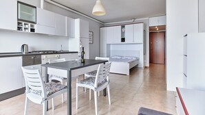 A modern kitchen with white cabinets, a dining table with chairs, a bed with a white headboard, and a pendant light. - Lydie apt. exclusive holigarda (Desenzano del Garda)