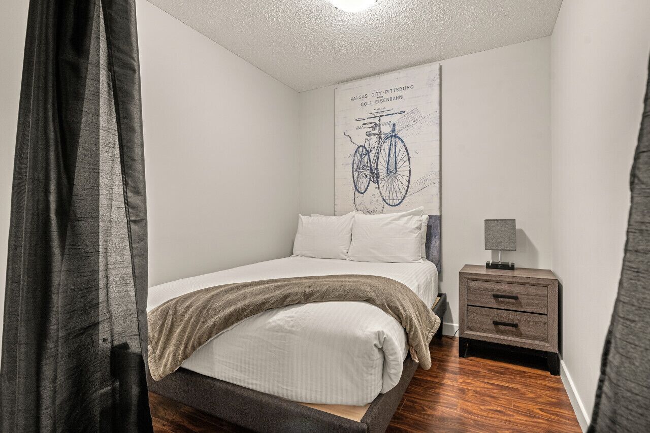 Quarto com cama, mesa de cabeceira e ilustração de bicicleta na parede.