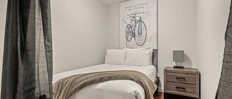 A bedroom with a bed, a nightstand, and a wall-mounted bicycle illustration.