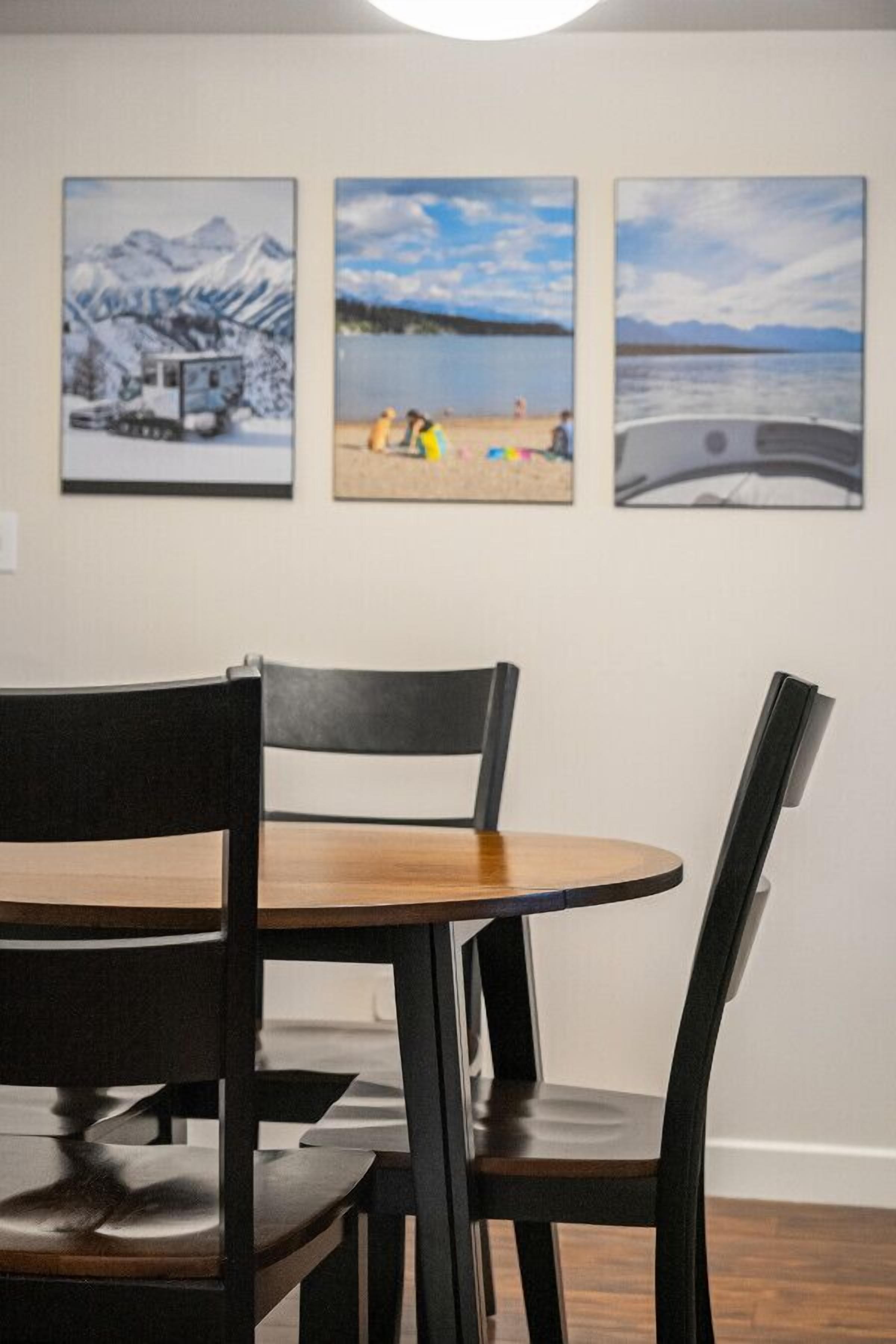 Een eetruimte met een ronde tafel en vier stoelen, drie ingelijste landschapsprenten aan de muur, en een houten vloer.