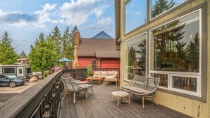A wooden deck with outdoor furniture, a red house in the background, and a clear sky. - Cedar & Sage | Hot Tub | A-Frame | Family Friendly (Radium Hot Springs)
