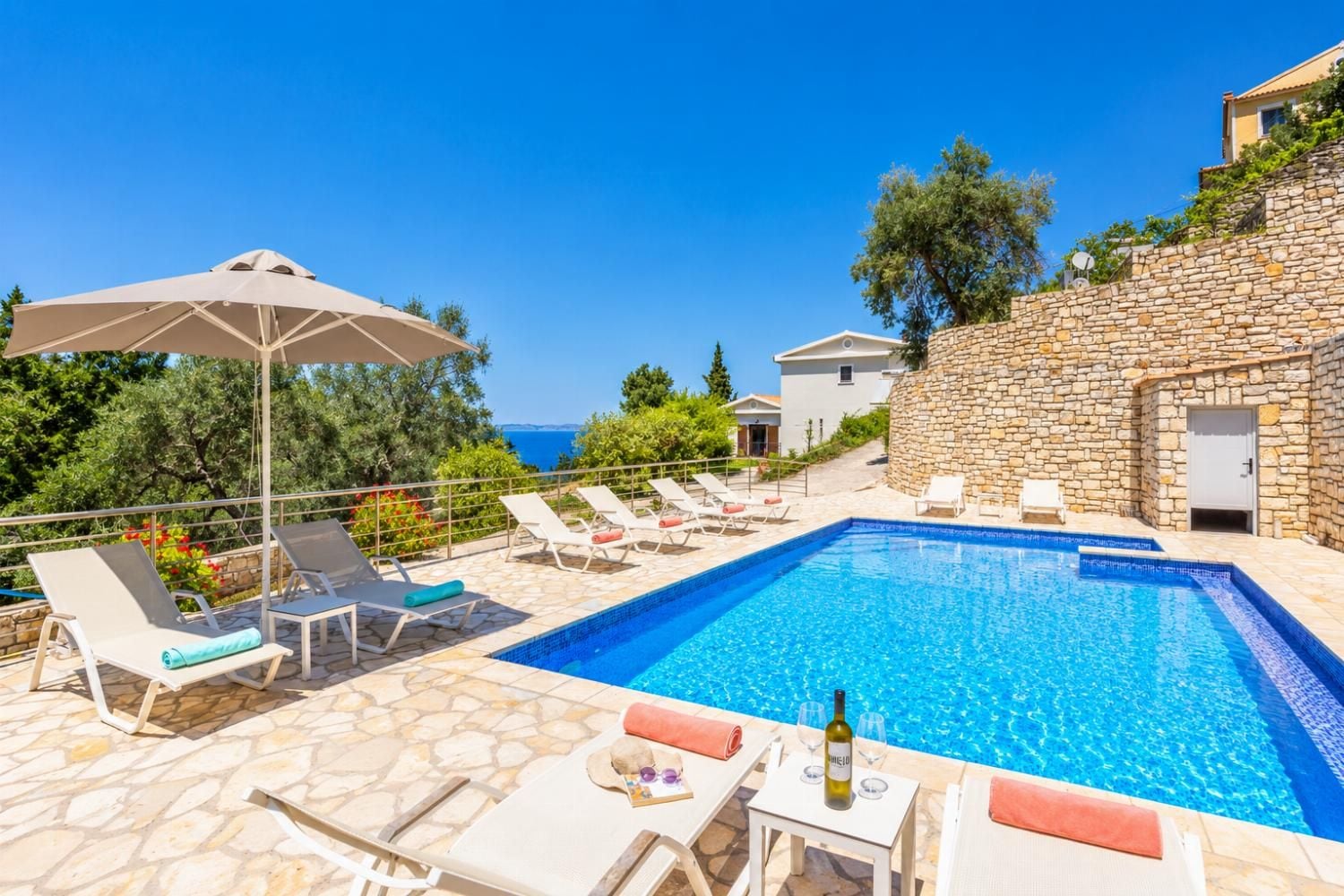 Ein Pool mit Liegestühlen und einem Tisch, umgeben von Steinmauern und Blick auf das Meer.