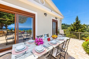 A dining table set for six with a view of the sea, outdoor seating, and a stone patio.
