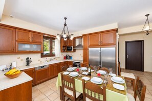 A kitchen with wooden cabinets, a stainless steel refrigerator, a dining table set for four, and a chandelier.