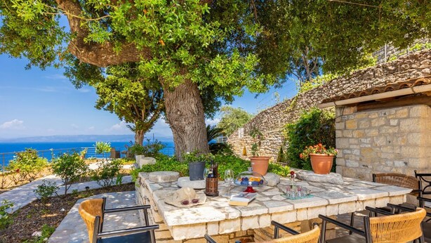 Un espacio de comedor al aire libre con mesas de piedra y sillas de mimbre, con vistas panorámicas al mar.