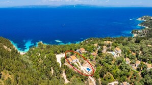 An aerial view of a coastal property with a swimming pool, surrounded by dense greenery and a clear view of the sea.