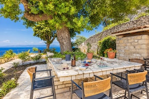 An outdoor dining area with stone flooring, wicker chairs, a table set with a wine bottle, glasses, and a book.