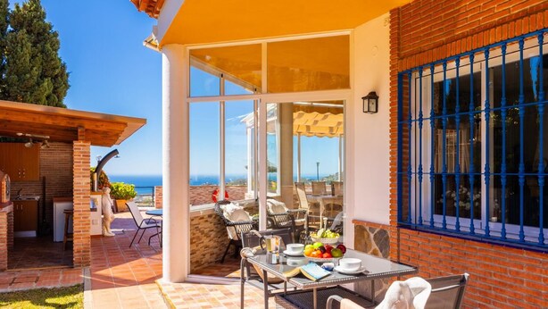 Terrassa exterior amb taula preparada per dinar, zona de barbacoa i vista al mar.