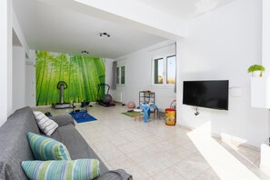 Un salon moderne avec un canapé gris, du matériel de sport, un téléviseur et une grande fenêtre.
