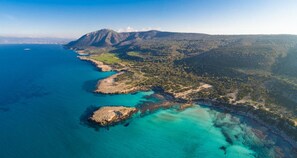 Vista aérea de un paisaje costero con una montaña destacada, aguas azules cristalinas y vegetación verde.