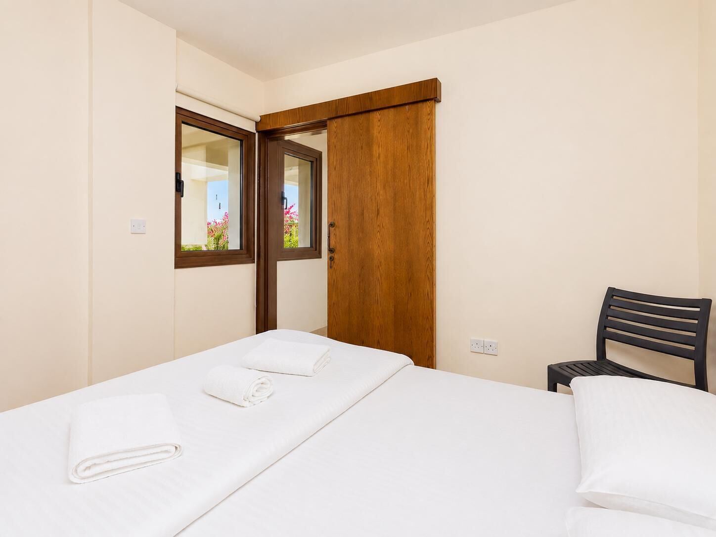Een slaapkamer met een bed, een stoel, een houten deur en een raam.