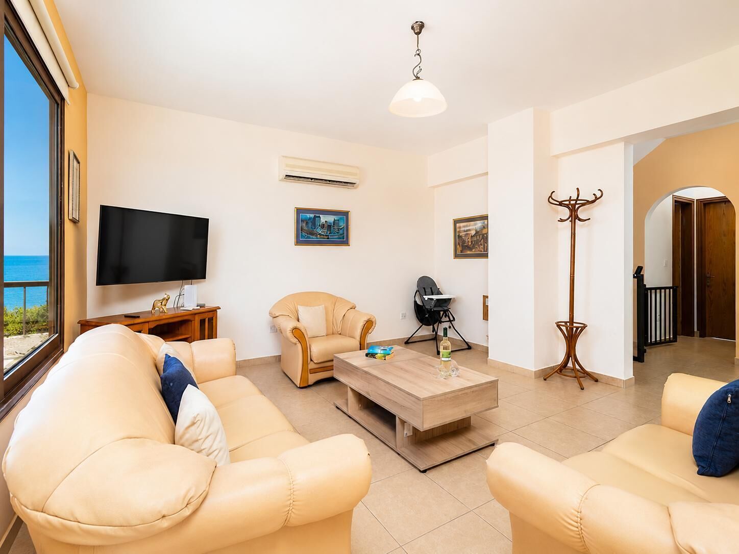 A living room with a sofa, armchair, TV, and artwork.