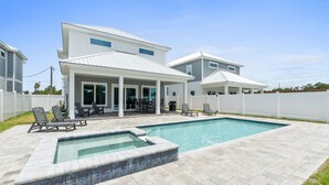 Une maison moderne à deux étages, dotée d’une piscine, de mobilier de jardin et d’un espace extérieur aménagé et abrité.