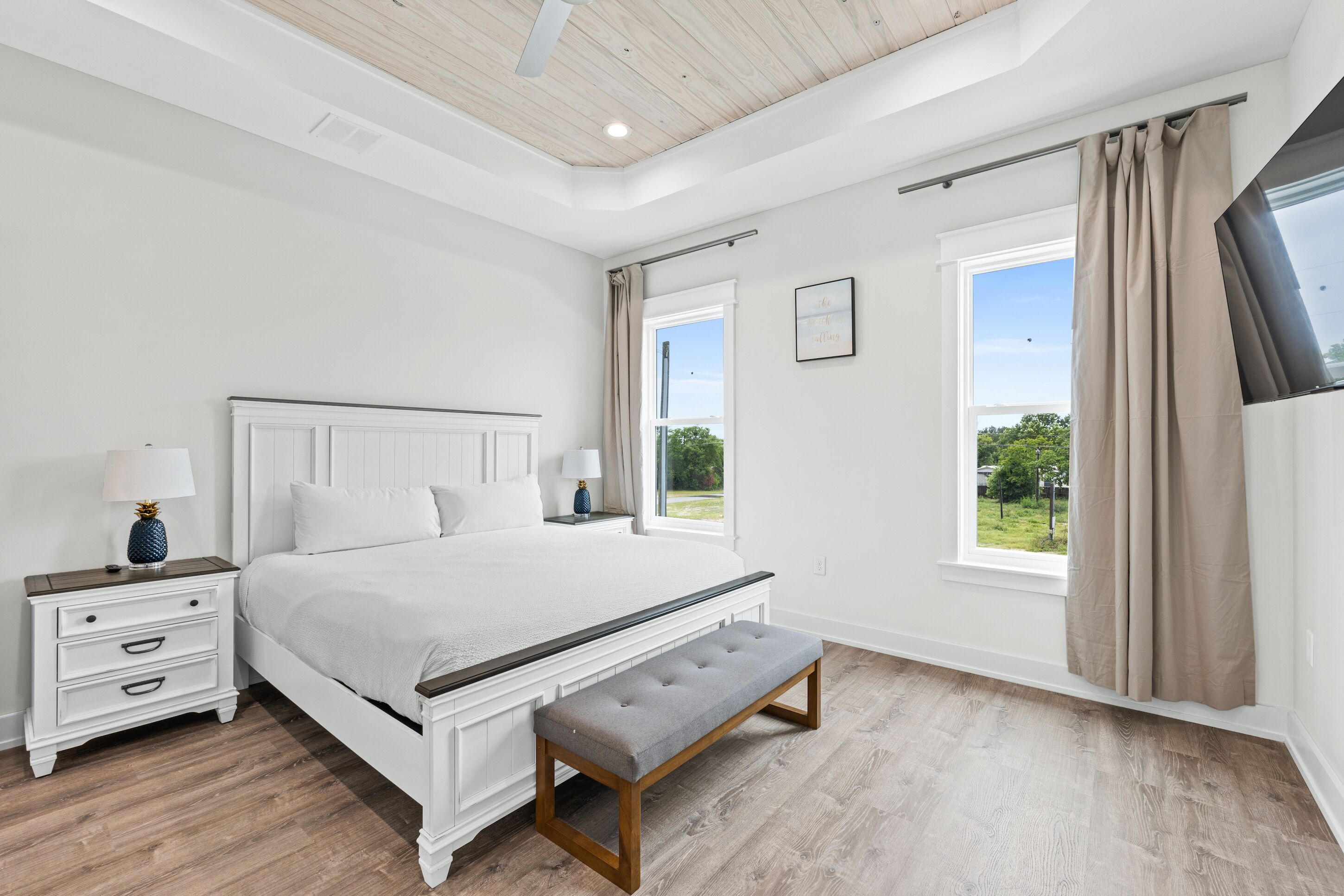A bedroom with a large bed, bedside tables, a bench, and a view of the outdoors.
