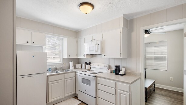 A kitchen with white cabinets, a stove, a microwave, and a sink. - Cottage 5 - Smugglers Run (Ridgeland)