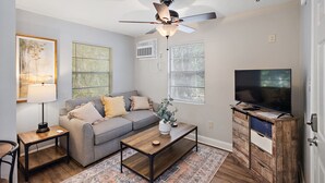 A living room with a sofa, coffee table, TV stand, ceiling fan, and artwork on the walls. - Cottage 5 - Smugglers Run (Ridgeland)
