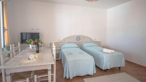 A room with a dining table, two beds with matching headboards, a television, and a decorative light fixture. - Superb Residenze del Golfo di Orosei Num2195 (Orosei)