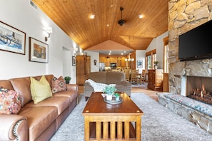 A living room with a stone fireplace, a wooden ceiling, and a kitchen in the background. - KBM Resorts | Town Pointe | 1 level with views of mountains, Walk to Main and Town Lift, Elevator access, Parking, A/C! TPC-301c (Park City)