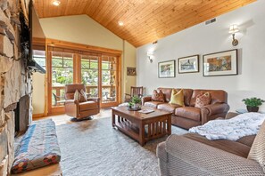 A spacious living room with a stone fireplace, wooden ceiling, and large windows offering a view of the outdoors. - KBM Resorts | Town Pointe | 1 level with views of mountains, Walk to Main and Town Lift, Elevator access, Parking, A/C! TPC-301c (Park City)