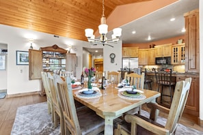 A dining area with a wooden table set for four, surrounded by wooden chairs. A chandelier hangs above the table, and a kitchen with wooden cabinets is visible in the background. - KBM Resorts | Town Pointe | 1 level with views of mountains, Walk to Main and Town Lift, Elevator access, Parking, A/C! TPC-301c (Park City)