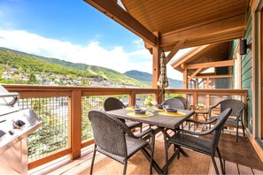 A covered outdoor dining area with wicker chairs and a grill, overlooking a scenic village and hills. - KBM Resorts | Town Pointe | 1 level with views of mountains, Walk to Main and Town Lift, Elevator access, Parking, A/C! TPC-301c (Park City)