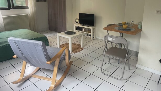 A room with a bed, a TV on a small table, a chair, and a table with cups and glasses. - Le Vert Galant (Morsang-sur-Orge)
