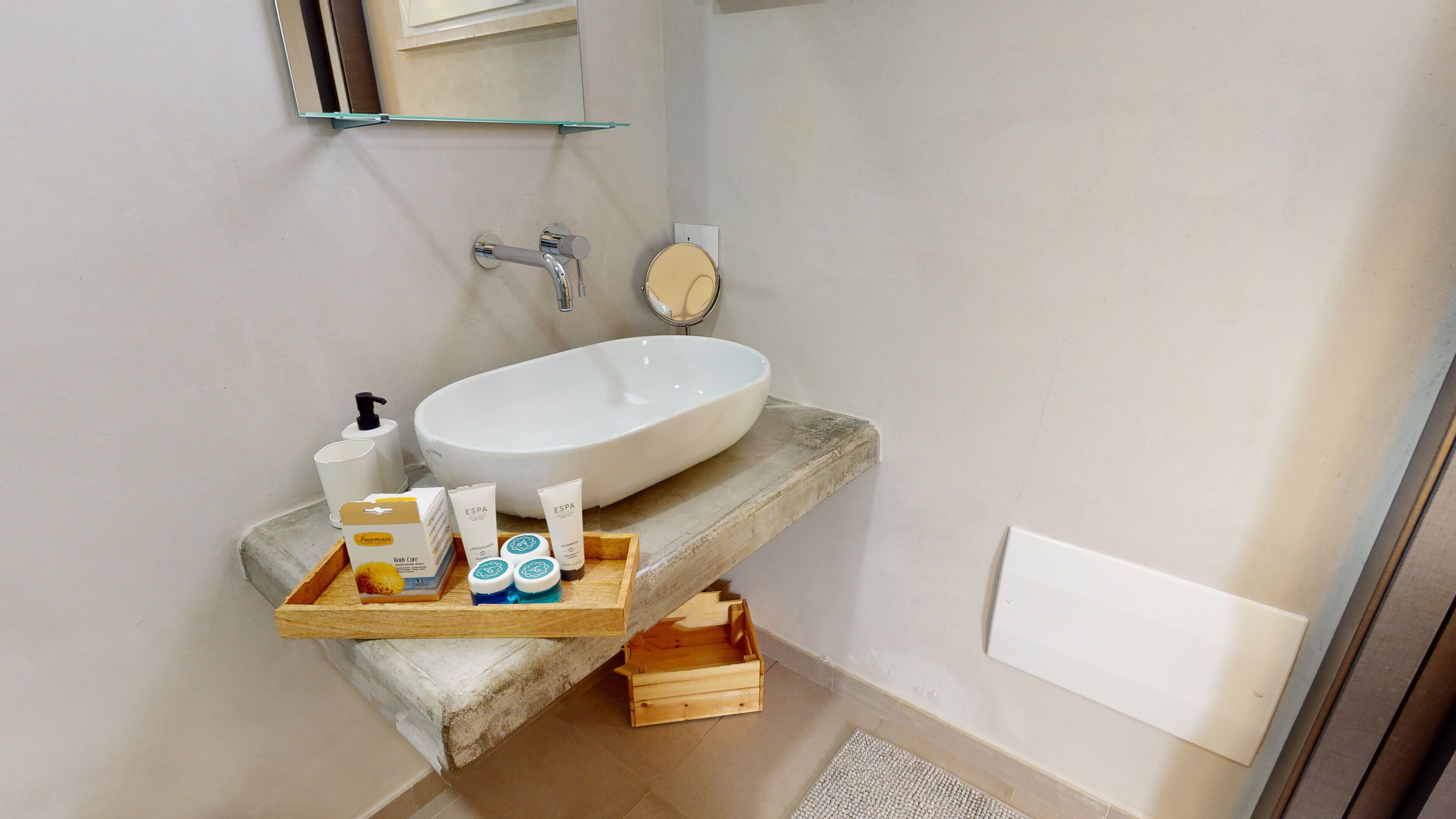 A bathroom with a white sink, a glass shelf with toiletries, and a wooden crate under the sink.