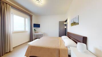 Camera d'albergo con un letto grande, una scrivania con una sedia, una TV a schermo piatto e un quadro appeso al muro.